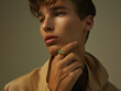 Fashionable portrait of a young man in a beige coat. Studio shot. in the style of gold and light emerald jewelry. Fashion magazine photo shoots.
