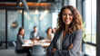 Young smiling successful businesswoman in formal wear standing in boardroom with arms crossed and looking at camera.In background her colleagues having meeting.