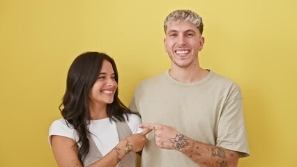 Poster - Excited, cheerful couple with a hopeful face expression, confidently pointing and smiling wide, showing teeth, expressing joy and positive emotion against isolated yellow background wall.