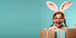Cute smiling girl wearing Easter bunny ears with shopping gifts with empty space for text over turquoise background