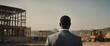 Black man in suit, seen from behind, looking at a construction site in Africa.