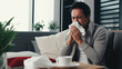 Colds, seasonal flu. An Asian guy with a runny nose sits on the couch at home. Guy sneezes, illness, respiratory disease. Bad feeling