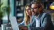 © Kostiantyn - A male and female professional in smart business attire engage in a collaborative task, sharing ideas over a laptop in a contemporary workspace.