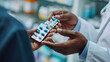 Close-up of a pharmacist's hand giving a blister pack of pills to a person, in a pharmacy setting with shelves of medical supplies in the background.