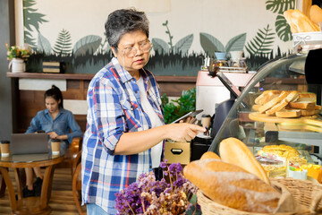 Wall Mural - Asian 60s healthy senior waitress worker woman or bakery shop small business retail owner happy checking bread stocks in cabinets for customer orders, elderly retired pensioner lifestyle working