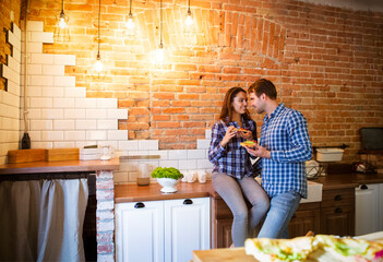 Young man and woman cooking and eating together at kitchen