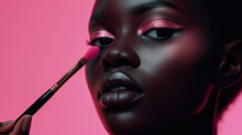 Close-up of the face of a young dark skin woman applying blush or powder to her face with a brush. Beauty shot.