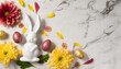 Top view of Easter decorations yellow and red flowers, petals ceramic easter bunny and colorful eggs on white marble background with copy space