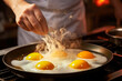 Close-up shot of frying pan on stove with fried eggs and cook's hand