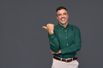 Wall Mural - Smiling older professional manager, happy middle aged business man entrepreneur, confident businessman looking at camera pointing finger aside presenting business ads isolated on gray background.