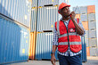 © offsuperphoto - African factory worker or engineer using walkie talkie and talking about work in containers warehouse storage
