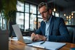 © Design Dynasty - Busy serious middle aged business man executive sitting at desk working on laptop writing notes. Professional businessman ceo manager using computer for elearning or management in modern,Generative AI