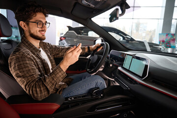 Wall Mural - Man holding auto key sitting in automobile rejoicing car purchase in dealership