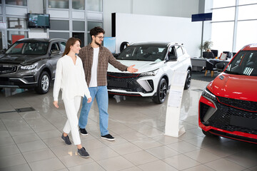 Wall Mural - Man and woman choose car in auto salon thinking about automobile model and color