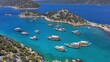 Excursion boats take a swimming break in Aquarium Bay Kekova in Turkey. Cinematic drone shot flying over a beautiful bay with turquoise water and tour boats. Many motorboats 