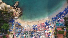Top Down View Of Sandy Beach With Turquoise Sea Water, Colorful Umbrellas And Swimming People. Crashing Waves In Golden Beach At Büyük Çakıl, Kaş Resort In Turkey. Drone Shot, Aerial View