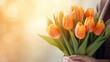 Women's hands holding a bouquet of orange or peach tulips for congratulations on Mother's Day, Valentine's Day, women's Day. Blurred background.