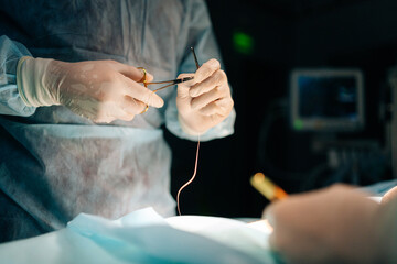 Wall Mural - Close-up hands of unrecognizable professional surgeon in hospital doing invasive surgical interventions. Closeup of surgeon and nurse use medical instrument or equipment in dark operating room.