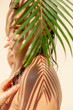 Nude woman stands in the shade of a palm branch....