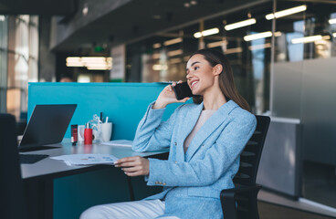 Smiling woman talking on mobile phone while sitting at table in office