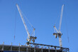 Two hoisting tower crane on the top section being construction of modern high skyscraper  building against blue cloudless sky