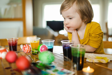 Wall Mural - Little boy watching Easter eggs getting dyed at home. Children painting colorful eggs for Easter hunt. Kids getting ready for Easter celebration.