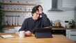 © mahirkart - Young man sitting in kitchen at home entering credit card number on tablet device for makes distant goods purchase. Credit card is declined or out of limit, feeling sad and unhappy