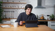 © mahirkart - Happy young man sitting in kitchen entering credit card number on tablet computer for makes secure easy distant electronic payment or buying goods