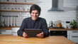 © mahirkart - Smiling man playing video game on a tablet computer while sitting in the kitchen at home. Excited concentrated male engrossed in interesting game with tablet device