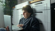 © mahirkart - Young man sitting on the floor in kitchen using, typing on laptop enjoying surfing internet, using social media, chatting with friends