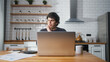 © mahirkart - Young man sitting in the kitchen with laptop pay bills, use calculator count expenses, make budget control, manage finances, review overdue loan payments feel stressed