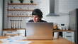 © mahirkart - Focusded man working at home in the kitchen working with his laptop, doing research. Busy freelancer working on modern tech notebook device
