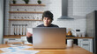 © mahirkart - Surprised university student sitting in the kitchen at home, looking laptop computer, studying, taking notes. Male student researching, study at home.