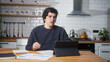 © mahirkart - Young man working at home in the kitchen working with his tablet computer, taking notes, doing research. Busy freelancer working on modern tech notebook device