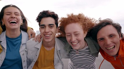 Wall Mural - Close-up shot laughing faces of young multiracial group friends looking at camera joyful. Generation z people community excited and hugging posing together for funny video outdoors on vacation. 