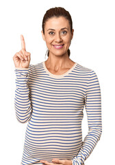 Pregnant middle-aged woman in studio setting showing number one with finger.