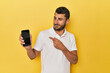 © Asier - Young Hispanic man shows phone screen smiling and pointing aside, showing something at blank space.