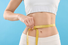 Slim Woman Measuring Waist With Tape On Light Blue Background, Closeup. Weight Loss