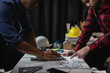 © MrAshi - Meeting and presentation in office with architects, construction engineers and workers looking at building models and blueprint plans on tables, industrial and real estate concepts.