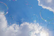 雲のある青空に浮かぶ虹色模様のシャボン玉
