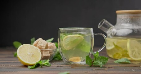 Wall Mural - putting slice of lemon into glass with natural organic herbal tea with glass teapot on a wooden table