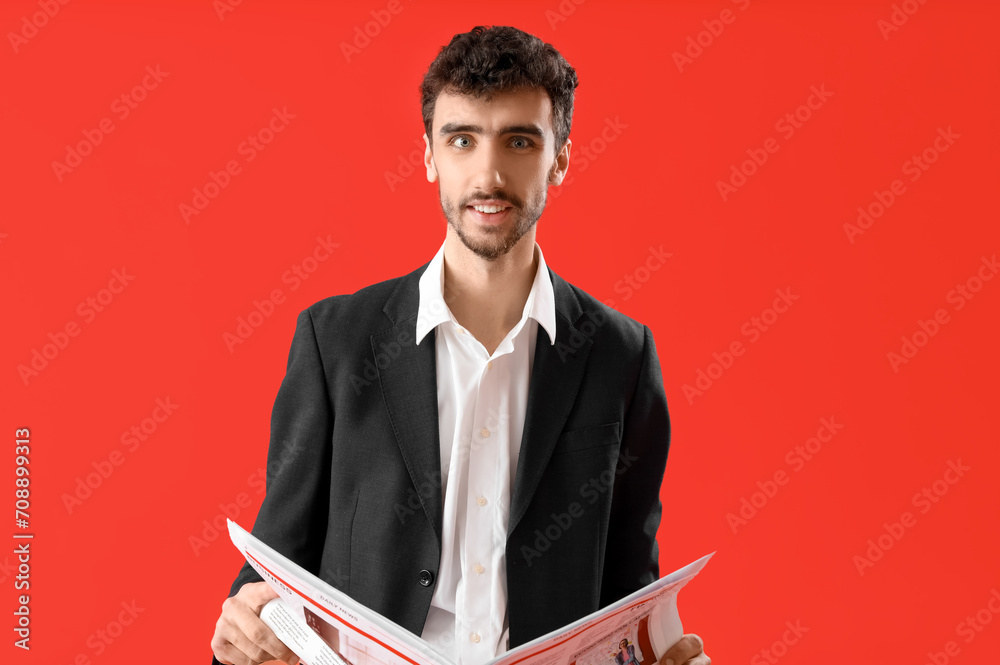 Young man in suit reading newspaper on red background