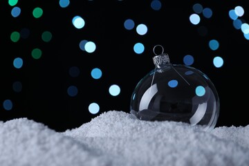 Wall Mural - Transparent Christmas ball on snow against blurred fairy lights, space for text