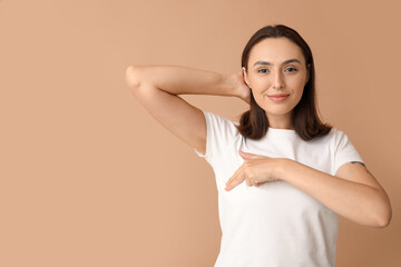 Poster - Young woman checking her breast on beige background. Cancer awareness concept