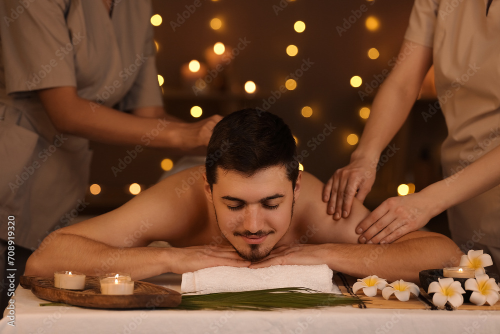 Young man getting massage from therapists in dark spa salon