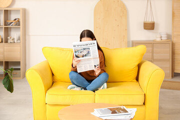 Sticker - Young woman reading newspaper on sofa at home