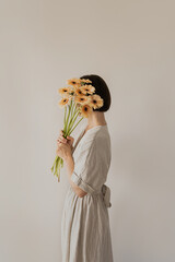 Wall Mural - Gerbera flowers bouquet in female hands. Young pretty woman in neutral tan sandy beige linen dress