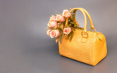 Yellow leather handbag with a bouquet of roses on a gray background