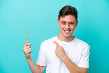 Wall Mural - Young Brazilian man brushing teeth isolated on blue background pointing to the side to present a product