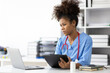 Serious african female doctor working stressed with paperwork in office.